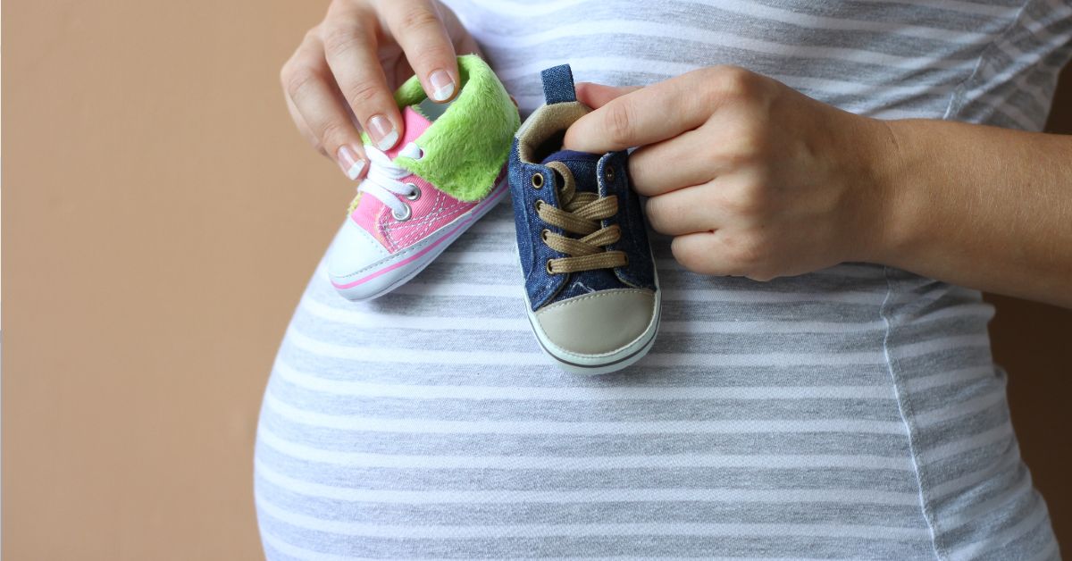 trudnica na stomaku drži rozu i plavu patikicu