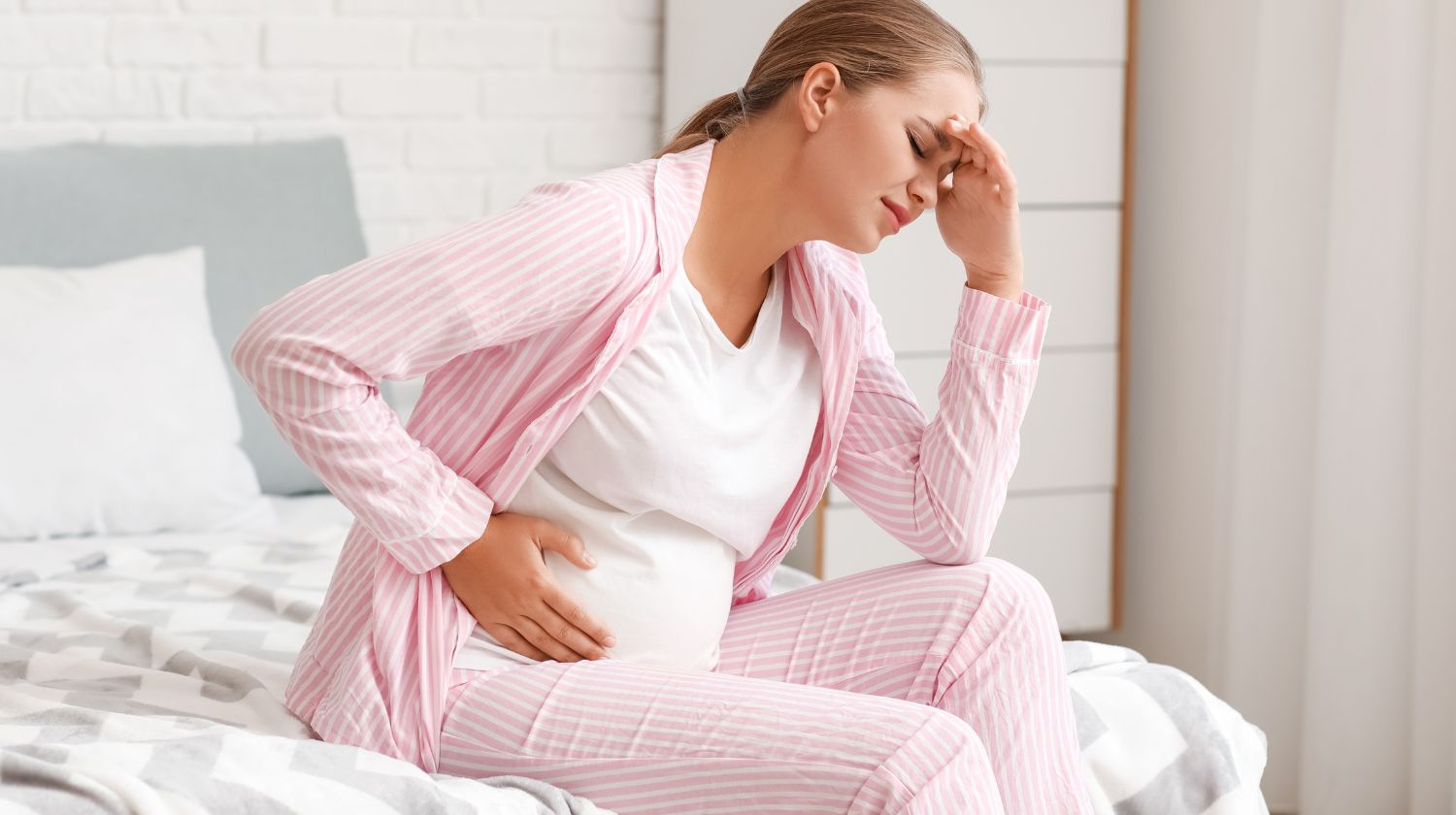 Trudnica sedi na krevetu loše se oseća drži se za glavu