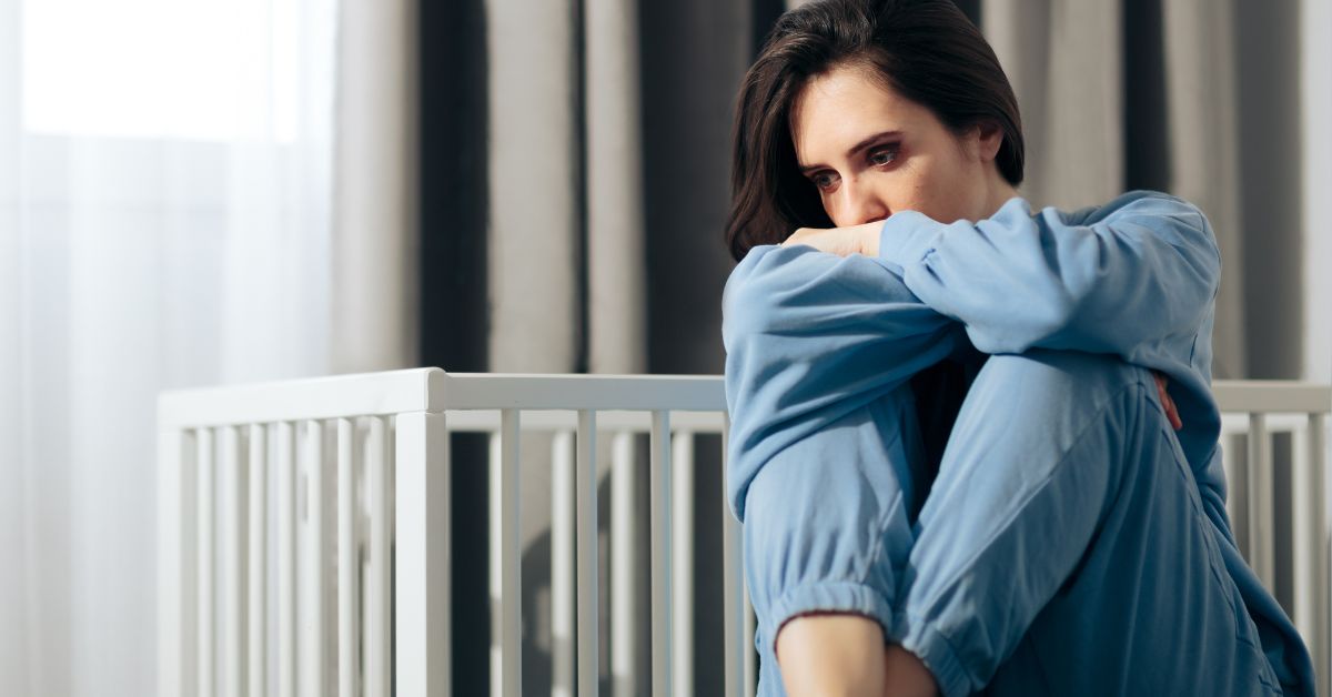 žena sedi neraspoložena pored dečijeg kreveta