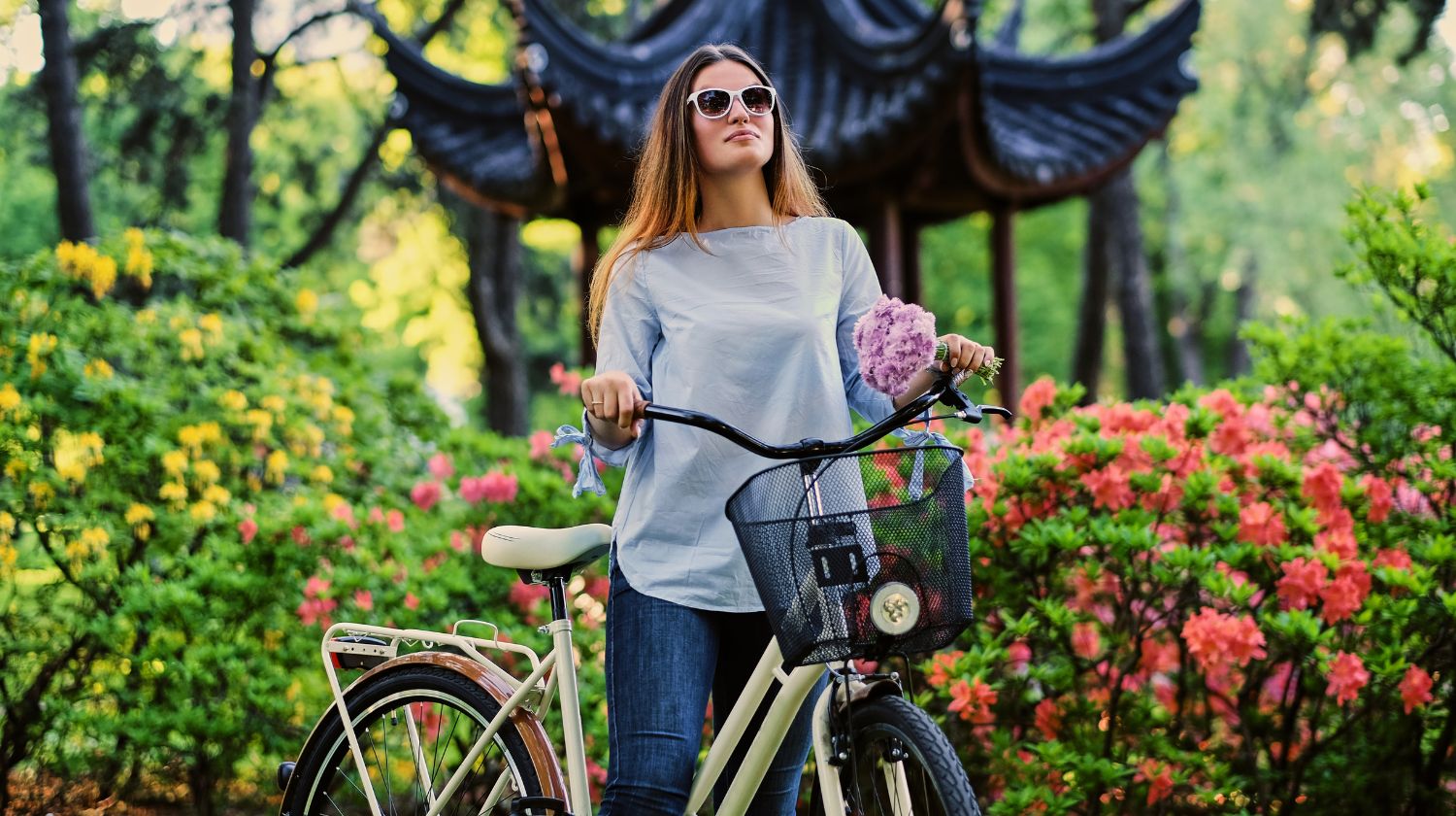 Žena stoji pored bicikla u cvetnoj bašti