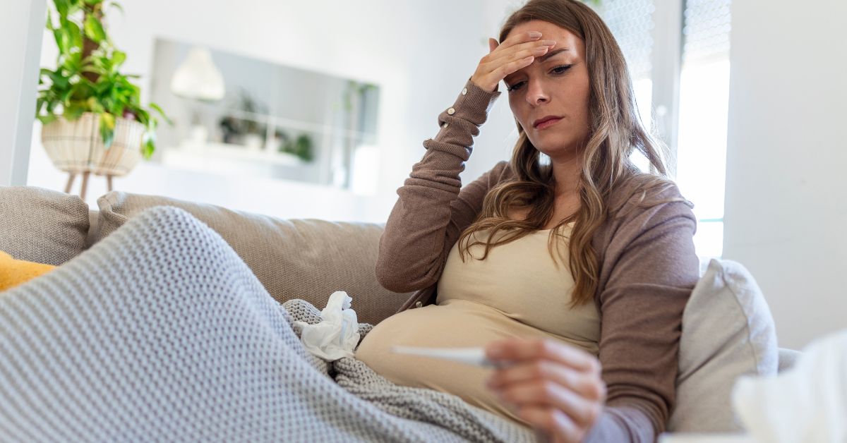 Trudnica sedi na kauču meri temperaturu