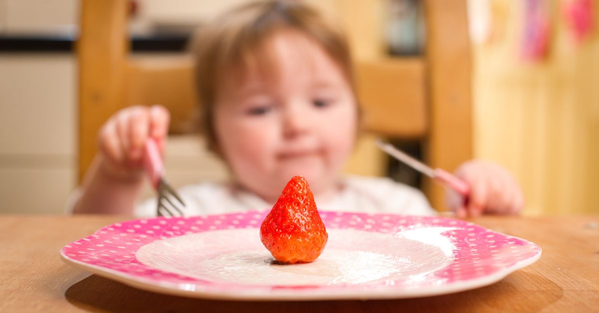 jedna jagoda na tanjiru i beba u pozadini