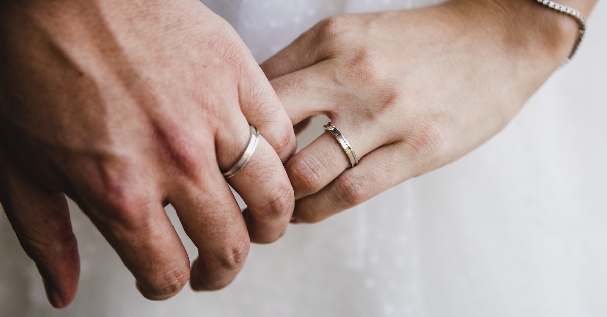 krupan kadar bračnog para koji se drži za ruke sa burmama na prstima