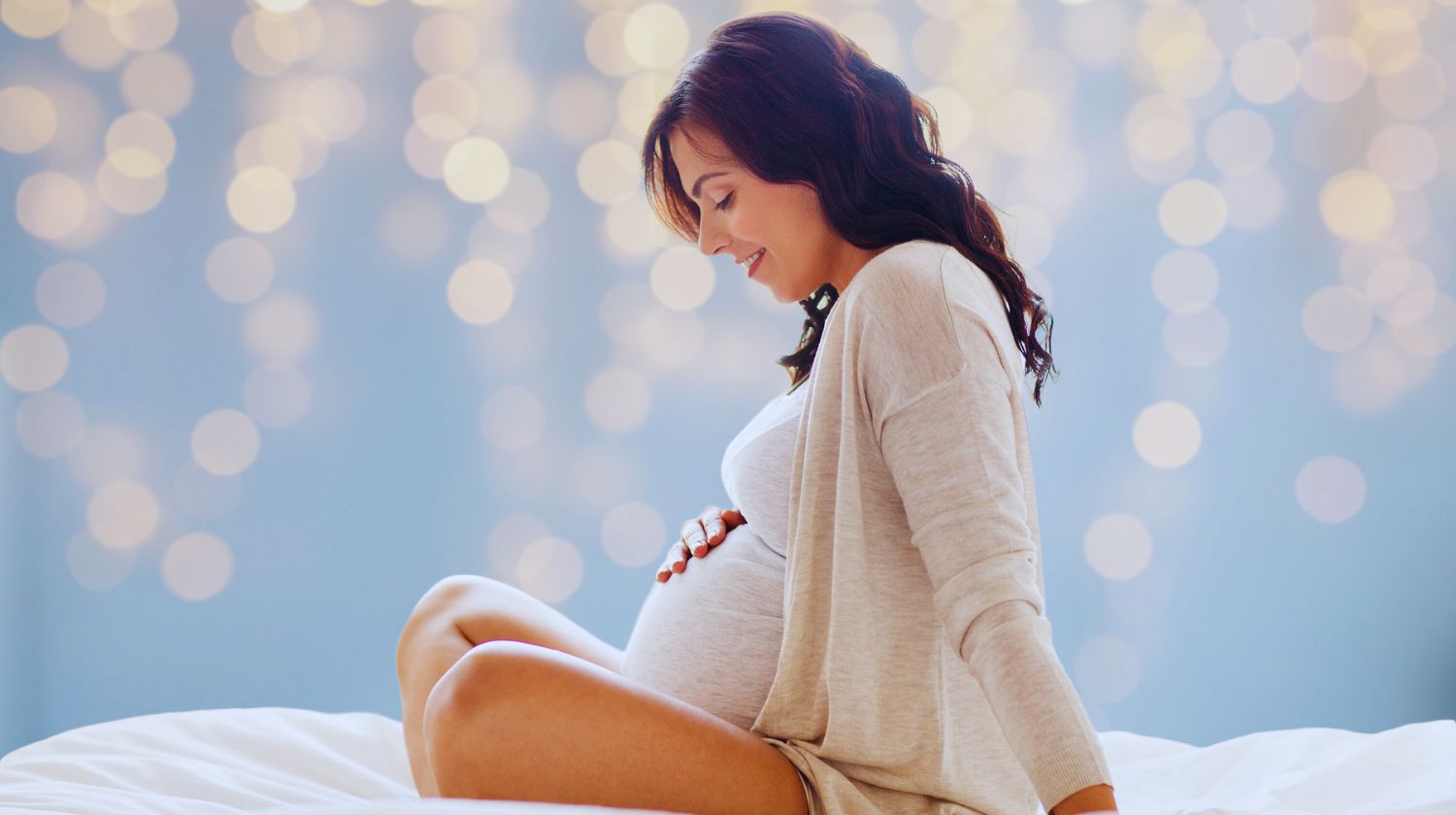 Trudnica sedi na krevetu i drži ruku na stomaku