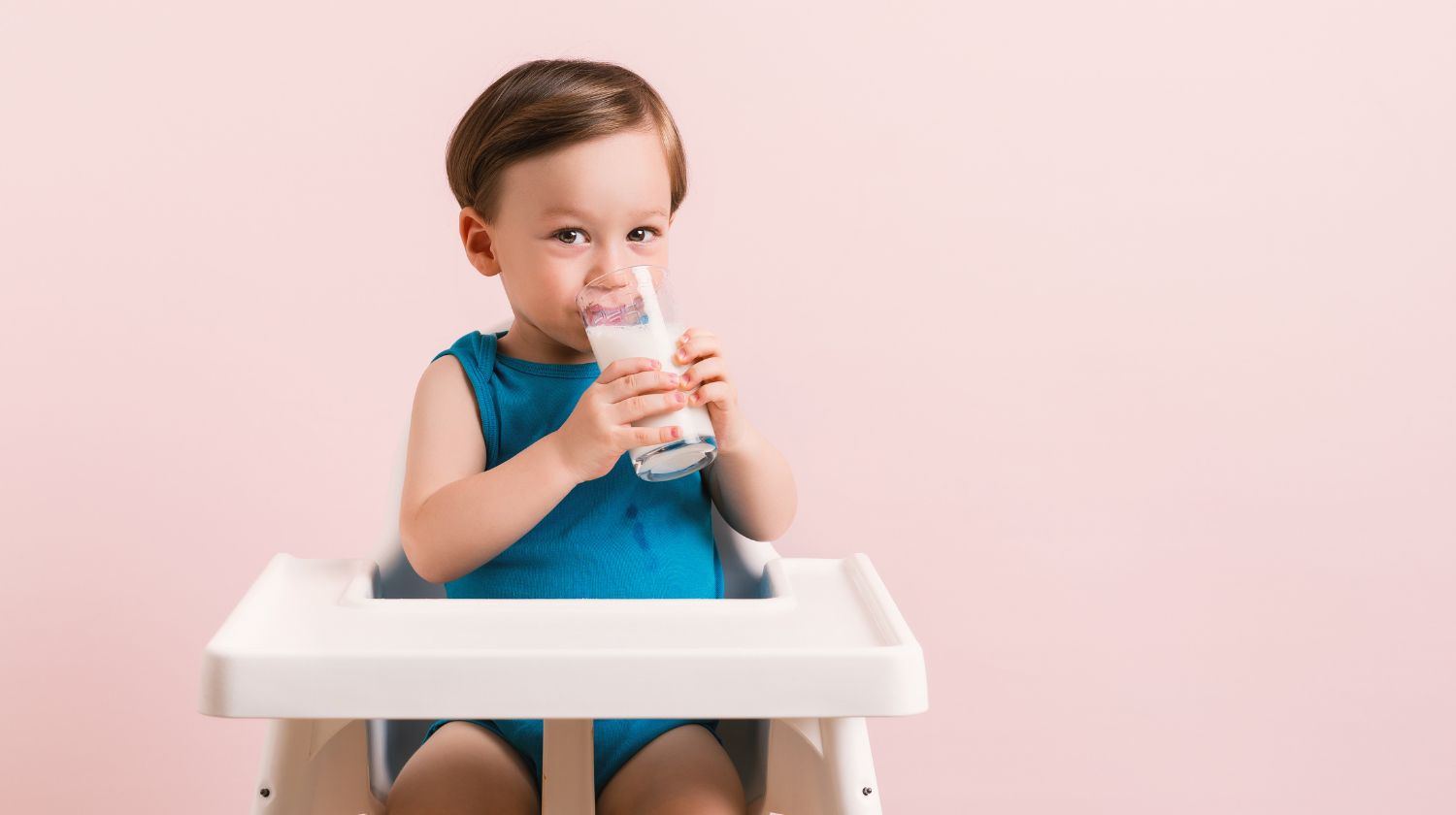 Malo dete pije mleko u stolici za hranjenje