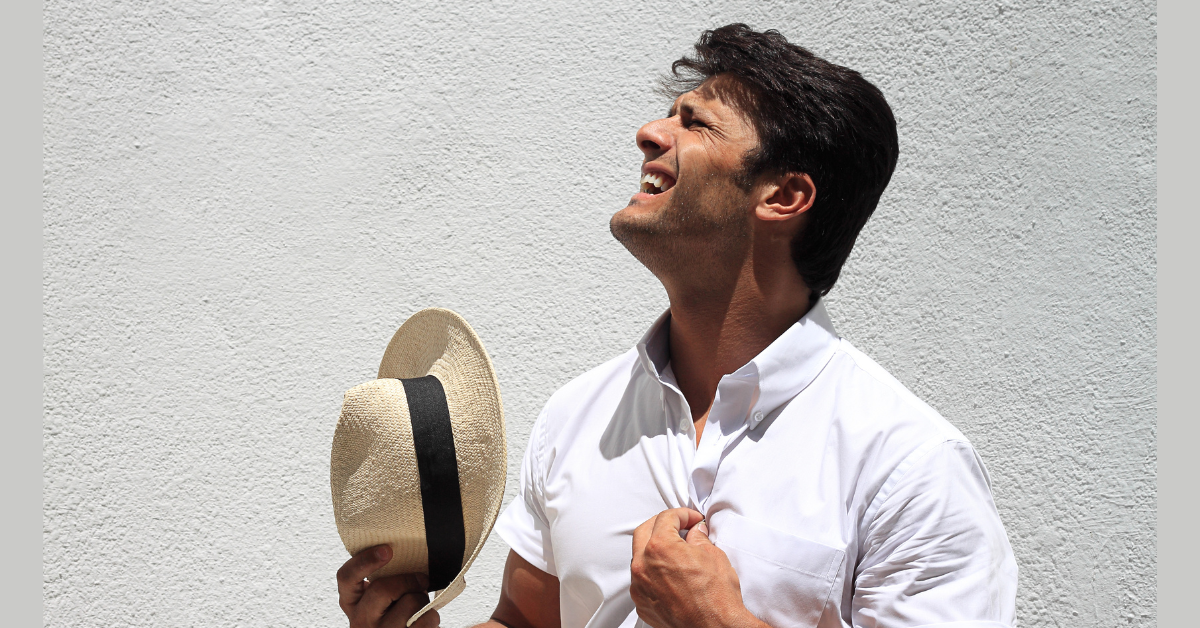 muškarac drži šešir na toplom vremenu u beloj polo majici 