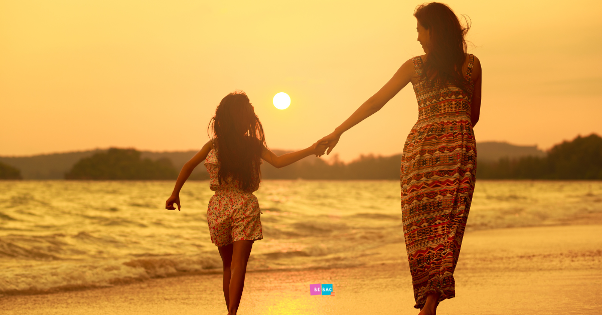 mama i ćerka se drže za ruke i šetaju na plaži