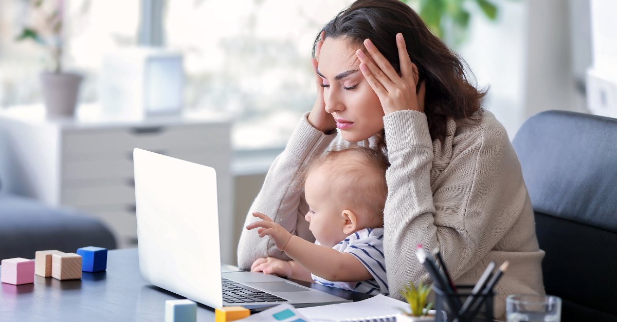mama se drži za glavu dok gleda u laptop a beba joj je u krilu