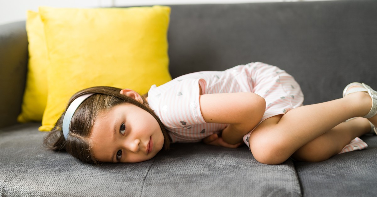 devojčica leži na krevetu boli je stomak