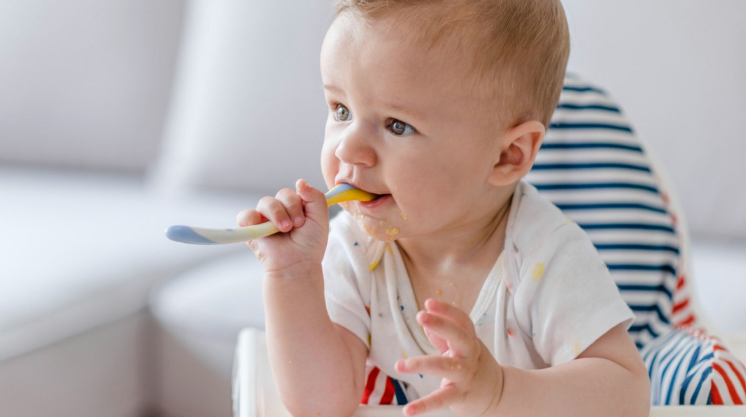 Beba sedi u stolici za hranjenje grize kašičicu