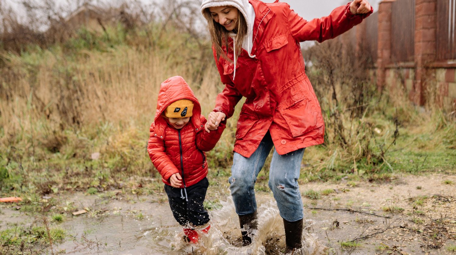 Mama i dete crveni kišni mantil skaču po baricama
