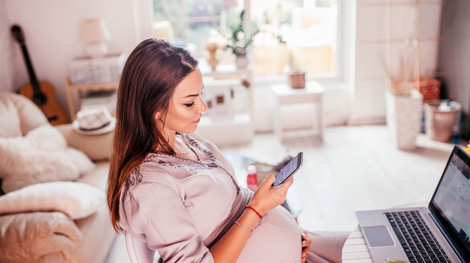 Trudnica sedi pored kompjutera i gleda u telefon