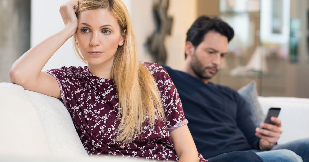 Žena okrenuta leđima muškarcu koji gleda u telefon