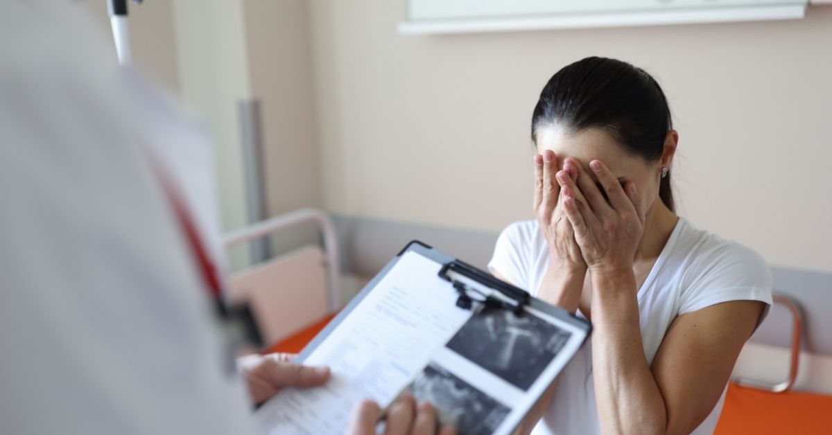 žena sa licem među rukama priča sa lekarom koji drži uz snimke