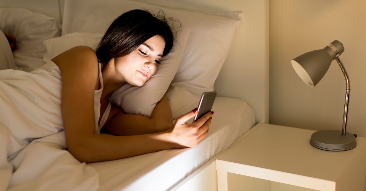 Žena leži u krevetu i skroluje po telefonu