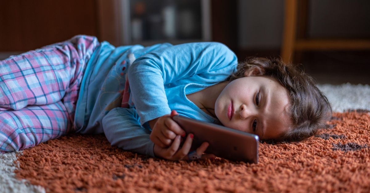 Devojčica leži na podu drži mobilni telefon