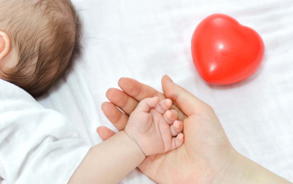 Mama drži bebinu ruku na dlanu, crveno srce pored